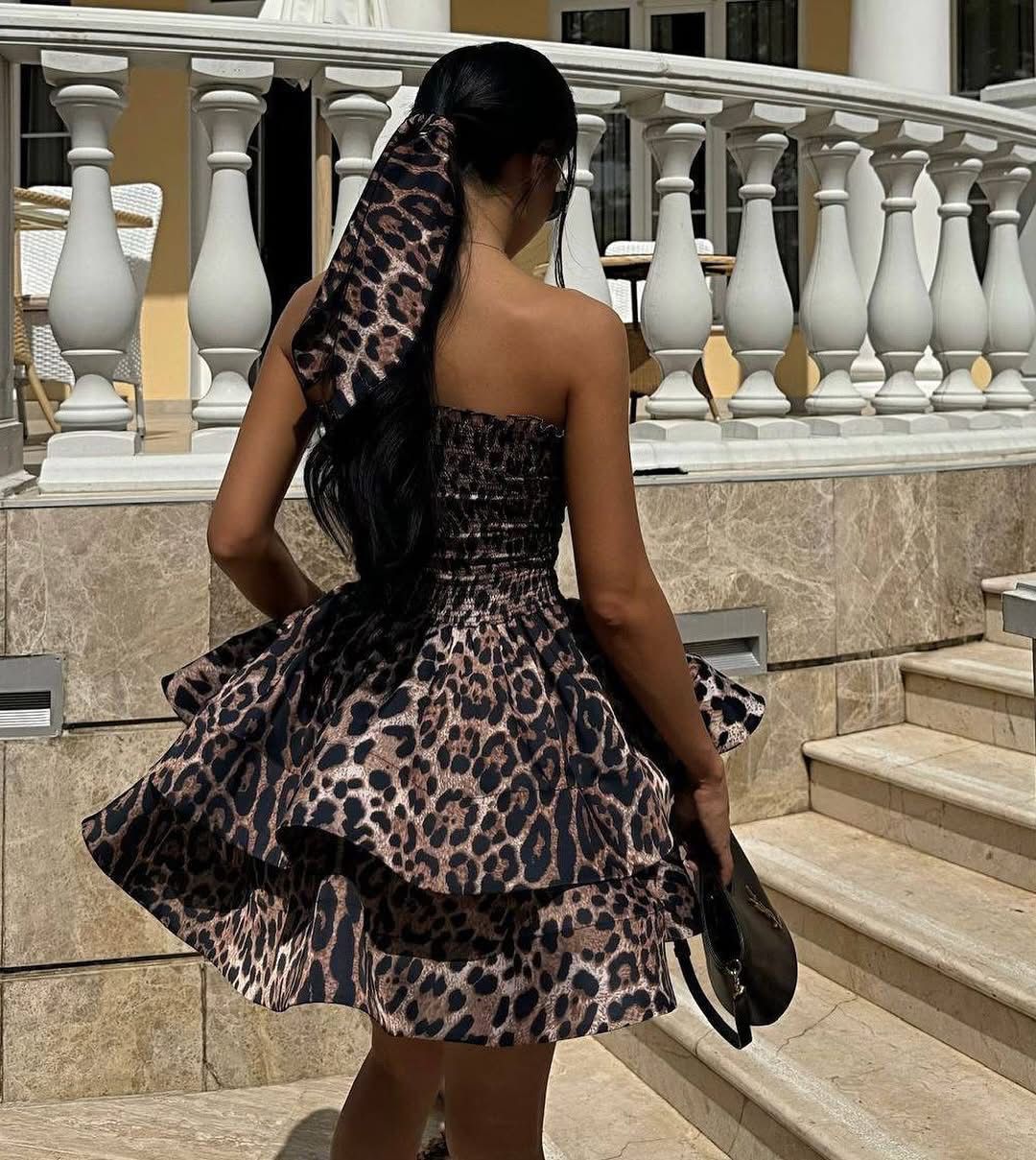 Woman in a leopard print dress standing on steps with a decorative railing.