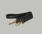 Black leather leash with gold hardware on a textured surface.