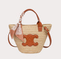 Woven straw bag with brown leather accents and a decorative bow on a white background