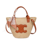Woven straw bag with brown leather accents and a decorative bow on a white background