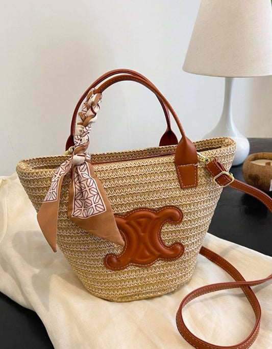 Woven straw bag with brown leather accents on a light surface.