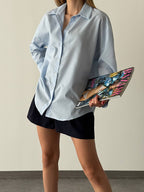 Woman wearing a light blue shirt and black shorts holding a colorful clutch.