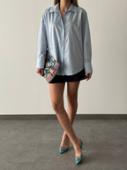 A stylish women's outfit featuring a shirt as the central piece. The shirt is light blue, with a classic design including a collar and button-up front.