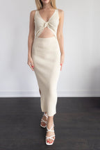 Woman wearing a cream-colored dress with a knot detail on a plain background