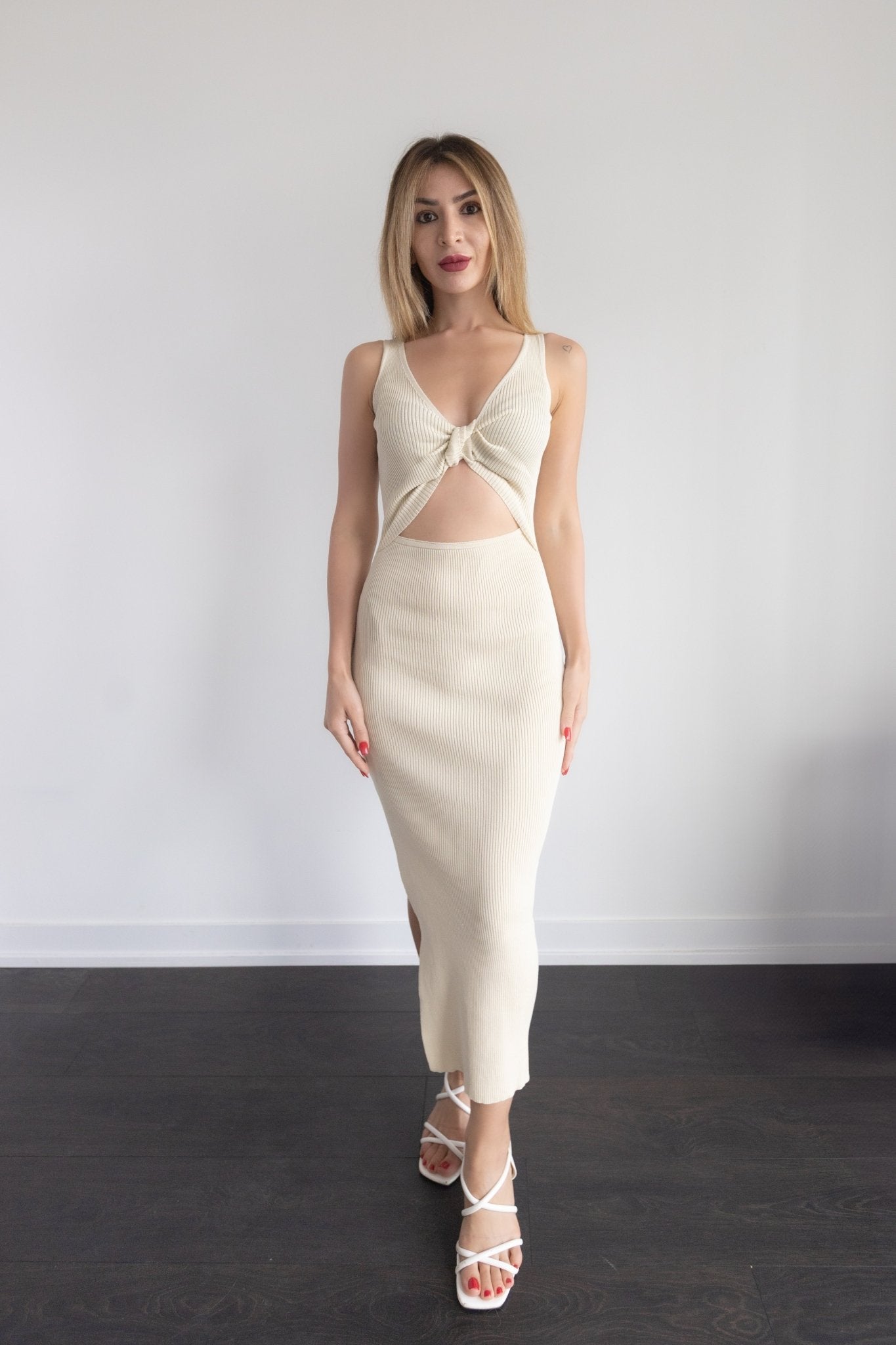 Woman wearing a cream-colored dress with a knot detail on a plain background