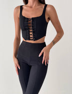 Woman wearing a black lace-up top and leggings on a light gray background