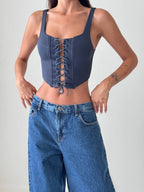 Woman wearing a blue lace-up crop top and blue jeans on a plain background
