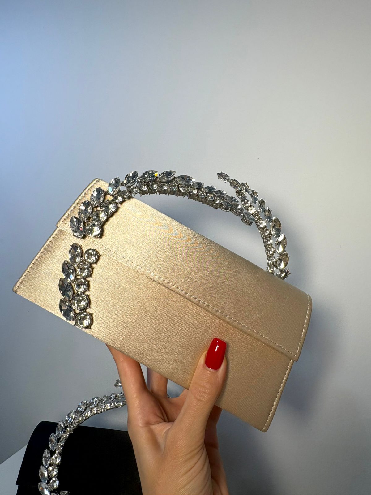 Beige clutch with decorative headband held by a hand against a neutral background