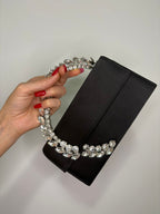 Black clutch with crystal handle held by a hand against a neutral background