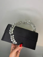 Black clutch with crystal handle held by a hand against a neutral background