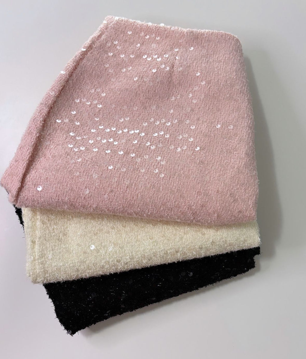 Collection of three skirts neatly stacked on top of each other, showcasing a variety of colors and textures. The top skirt is a soft pink with visible sequins sprinkled across its surface, giving it a subtle shimmer.