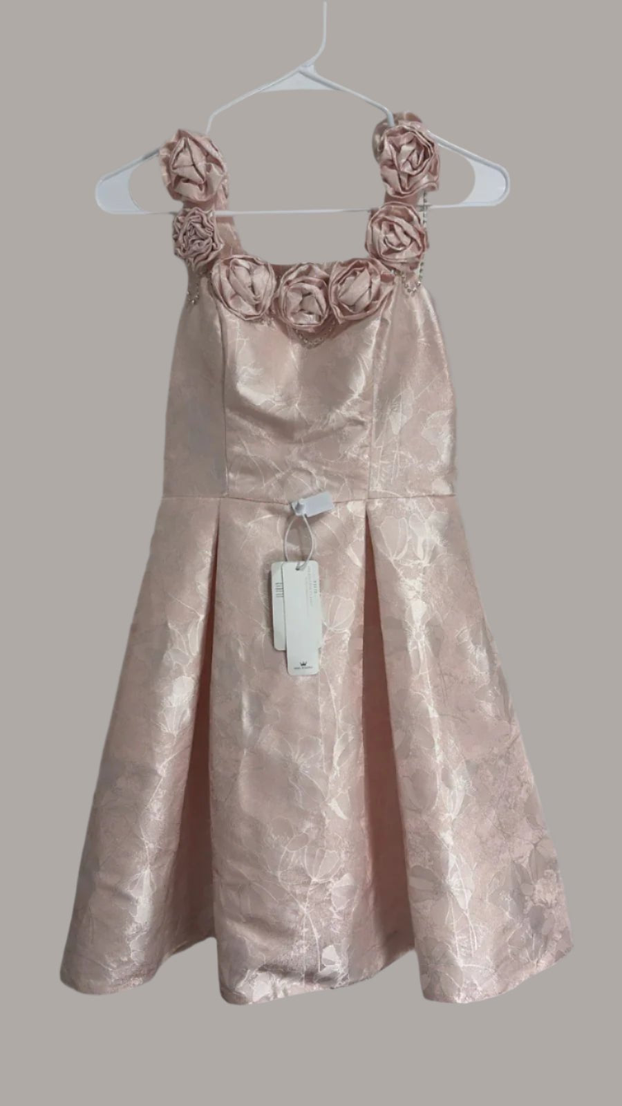 Pink dress with floral straps on a hanger against a white background