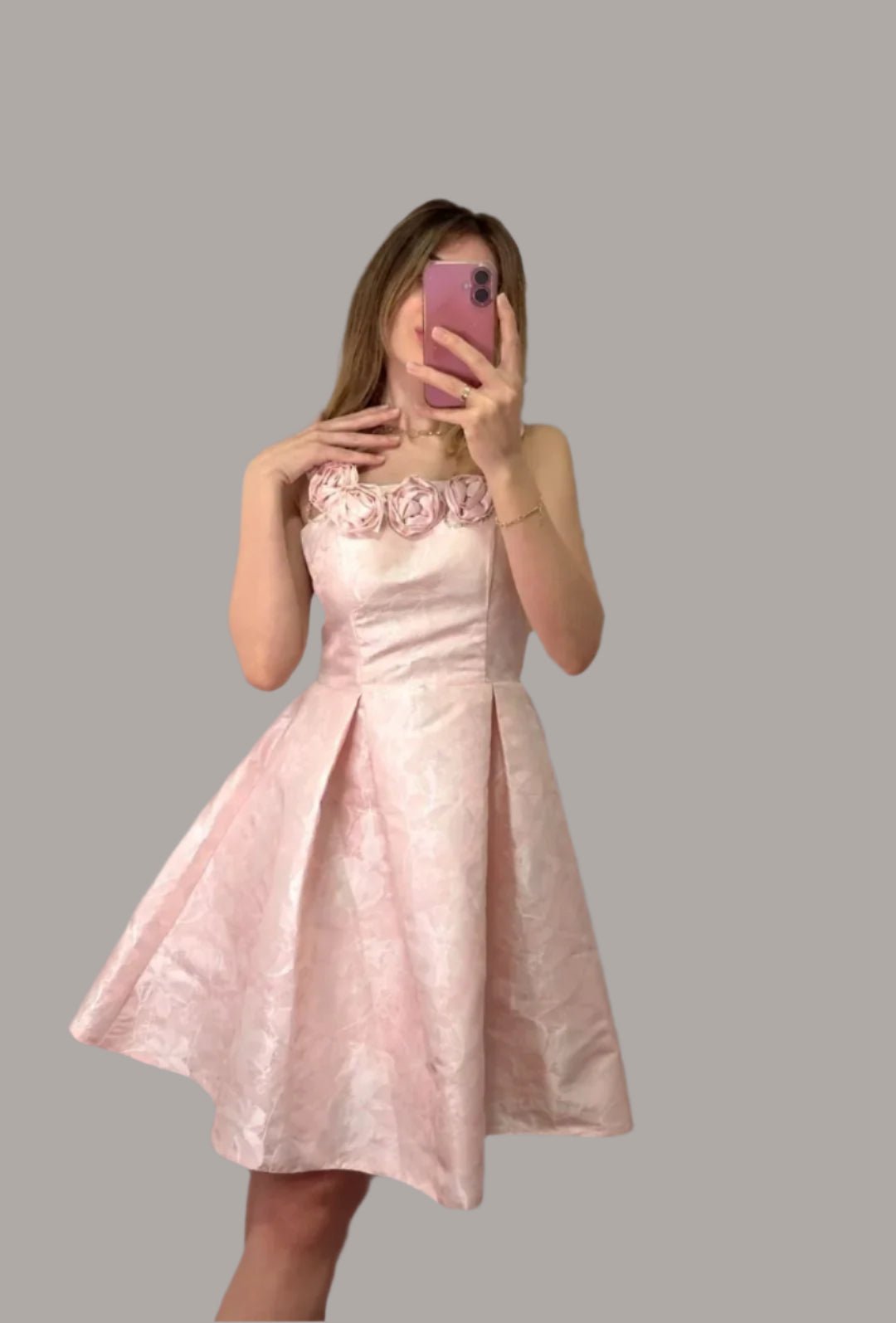 Woman taking a mirror selfie wearing a pink dress with a floral background