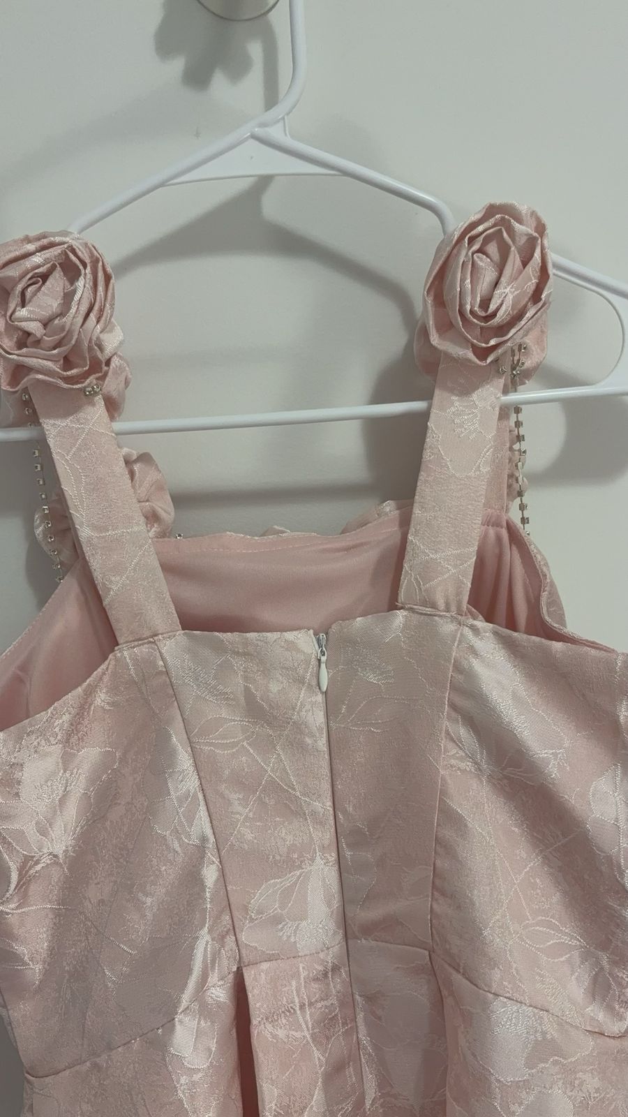 Pink dress with floral straps on a hanger against a white background