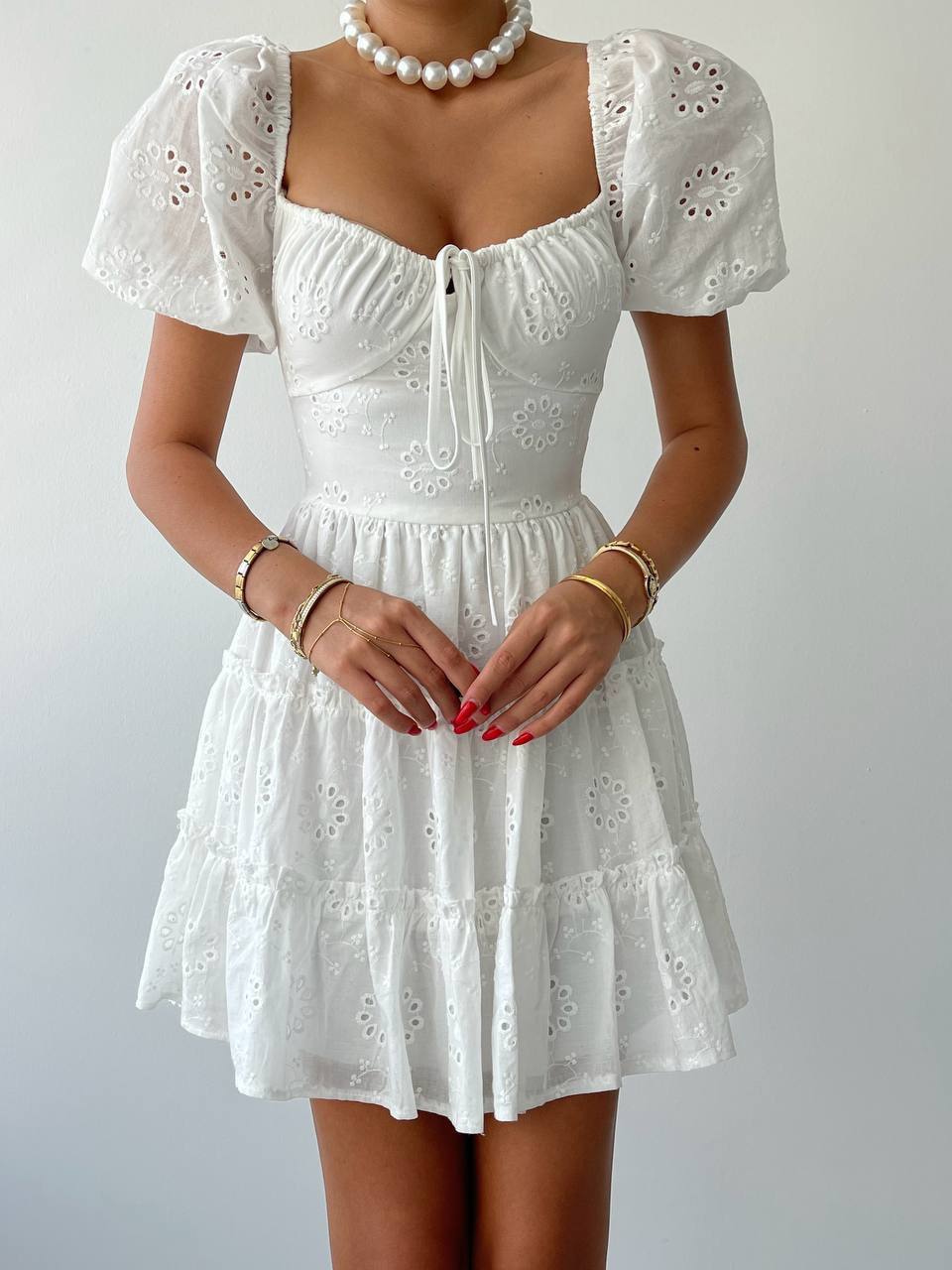 A woman wearing a white short-sleeved mini dress with lace details and a square neckline.