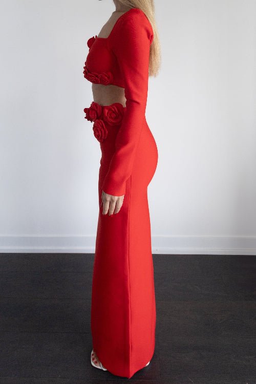 Woman wearing a red dress with floral details against a white wall.