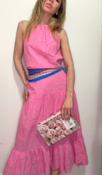 Woman wearing a pink dress with a blue belt and holding a clutch with floral design.