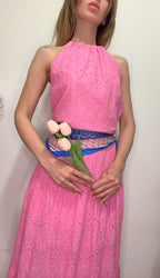 Woman wearing a pink dress with a blue belt, holding pink flowers against a plain background