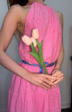 Woman wearing a pink dress holding tulips against a plain background
