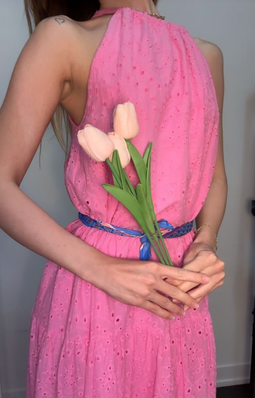 Woman wearing a pink dress holding tulips against a plain background