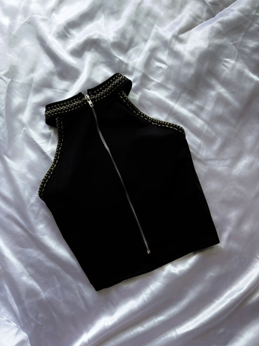 Black sleeveless top with a zipper on a white fabric background
