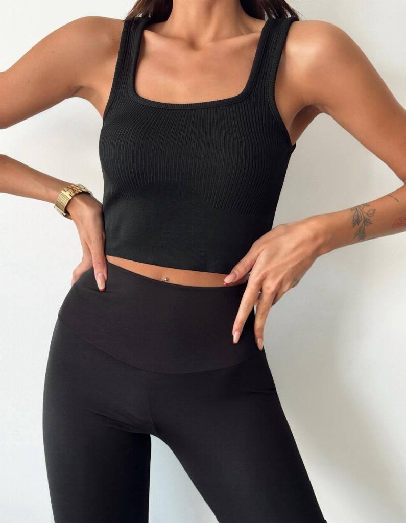 A woman wearing a black crop top and leggings, standing against a white background.