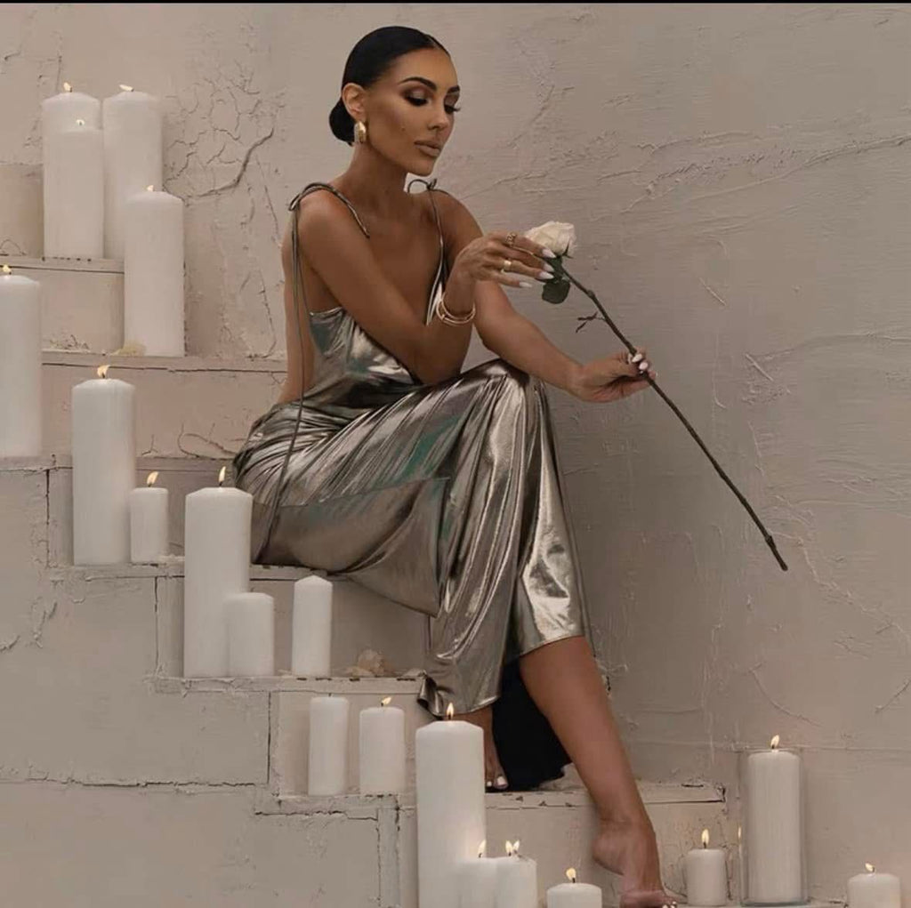 A woman seated on a step surrounded by candles, wearing a silver dress with a sleeveless top and long skirt.