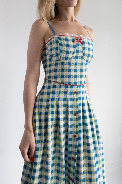 Woman wearing a blue and white checkered dress with red buttons on a plain background