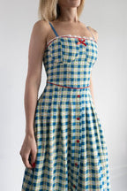 Woman wearing a blue and white checkered dress with red buttons on a plain background