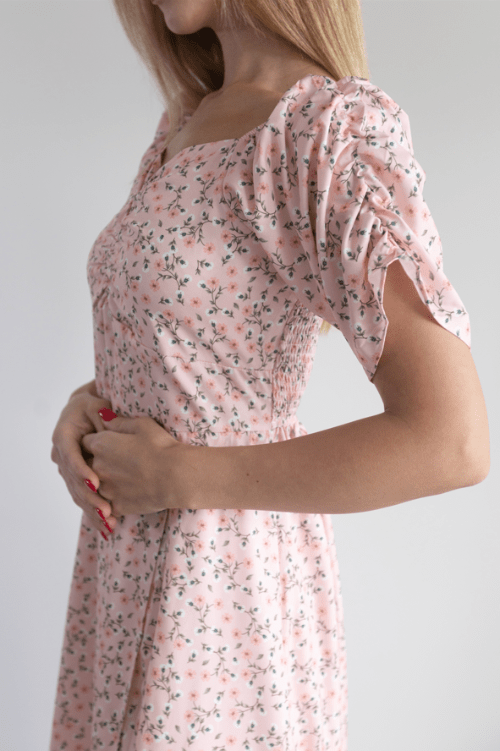 Woman wearing a pink floral dress with puff sleeves on a plain background