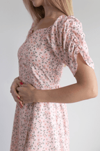 Woman wearing a pink floral dress with puff sleeves on a plain background