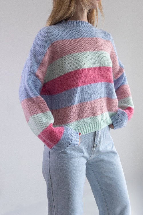 Person wearing a colorful striped sweater and light blue jeans against a plain background