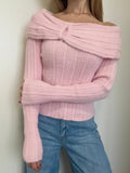 Person wearing a pink off-shoulder sweater and blue jeans against a plain background