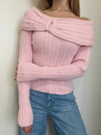Person wearing a pink off-shoulder sweater and blue jeans against a plain background