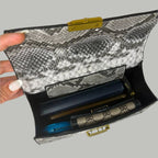 Snakeskin-patterned clutch bag with visible contents on a white surface.