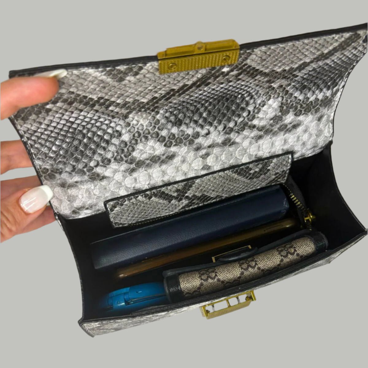 Snakeskin-patterned clutch bag with visible contents on a white surface.