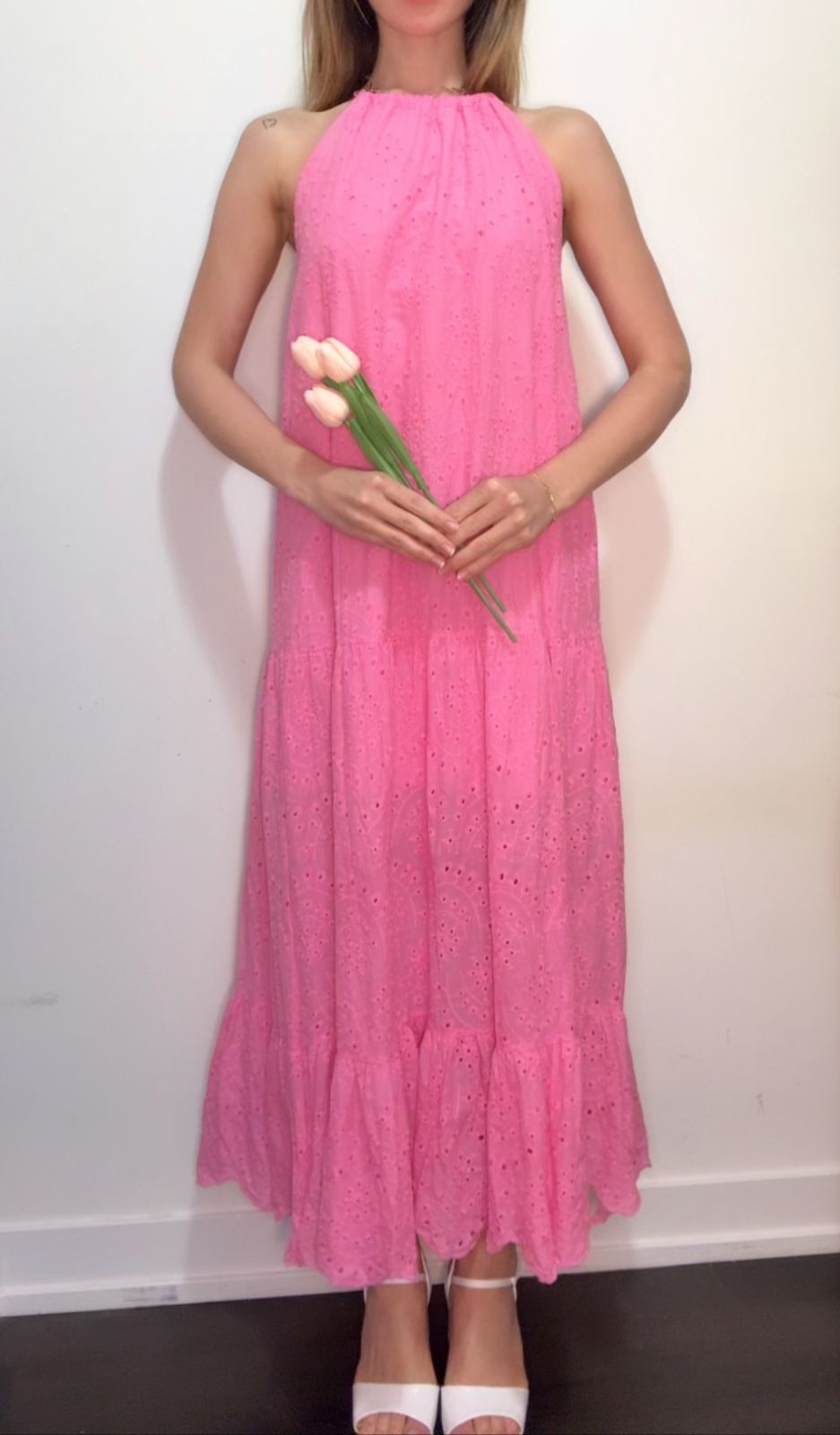 Woman wearing a pink dress holding pink flowers against a plain background