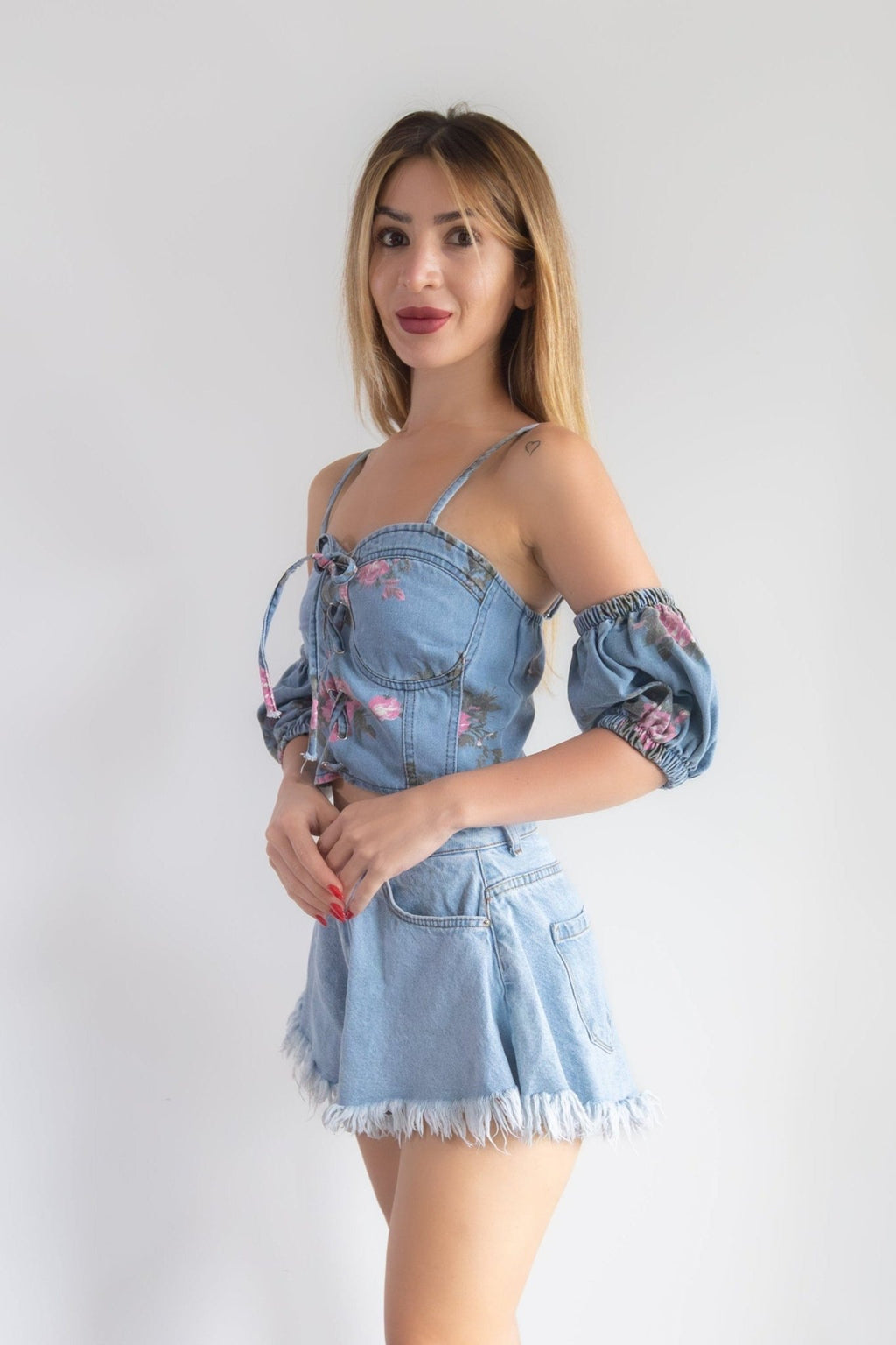 Woman wearing a denim outfit with floral details on a plain background