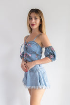 Woman wearing a denim outfit with floral details on a plain background