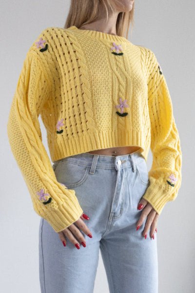 Person wearing a yellow knitted sweater with floral designs on a plain background